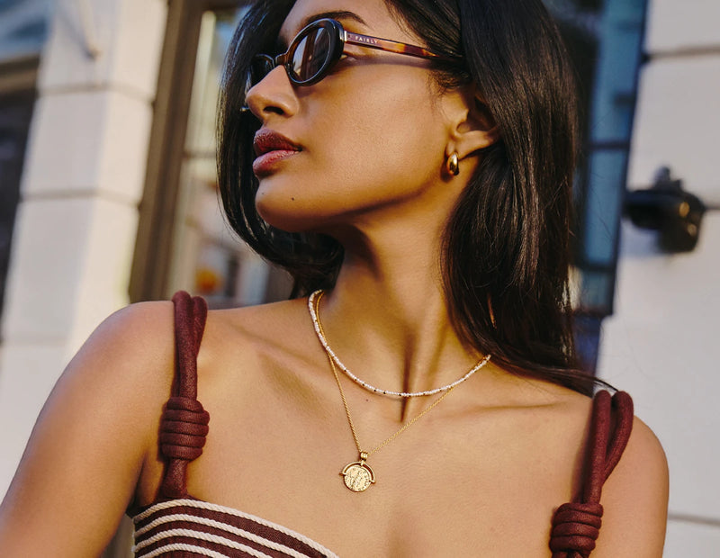 Woman wearing sunglasses and a gold roman arc necklace and micro pearl necklace