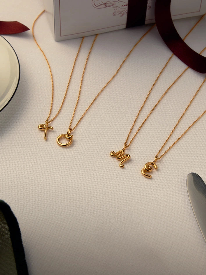Three gold necklaces with initial charms on a white surface