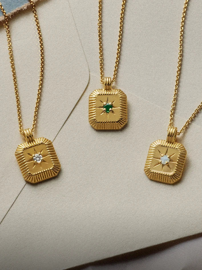 Three gold necklaces with initial charms on a white surface