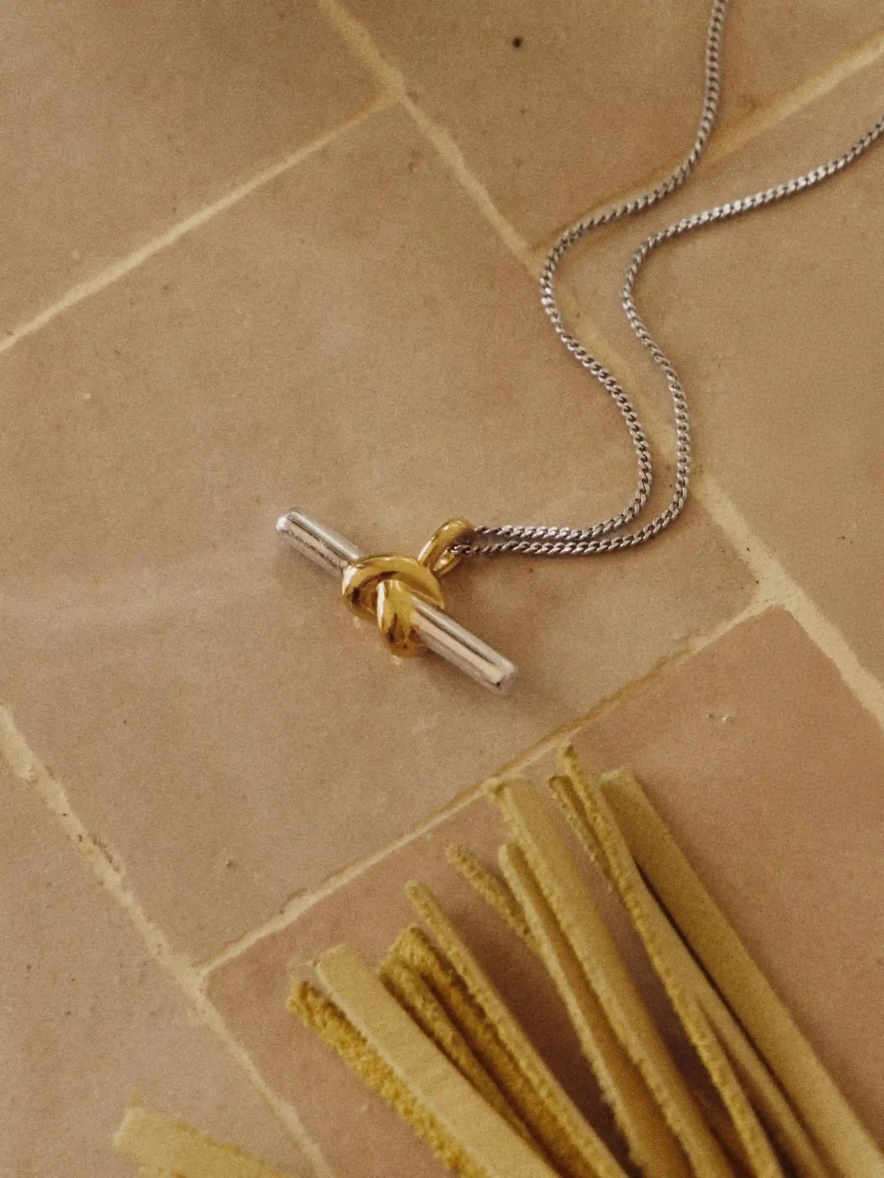 Gold and silver T-Bar Necklace  on a beige stone surface