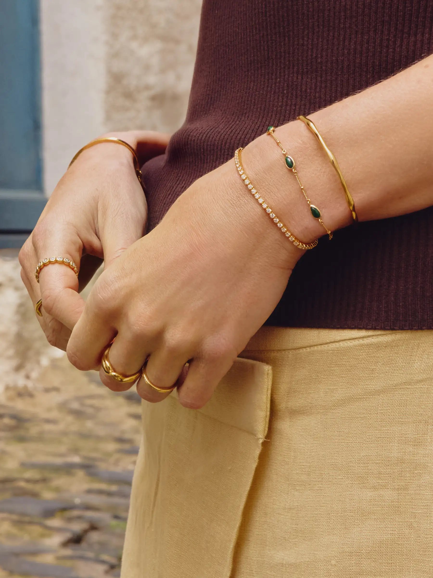 Close-up of hands wearing gold bracelets and rings with a blurred natural background